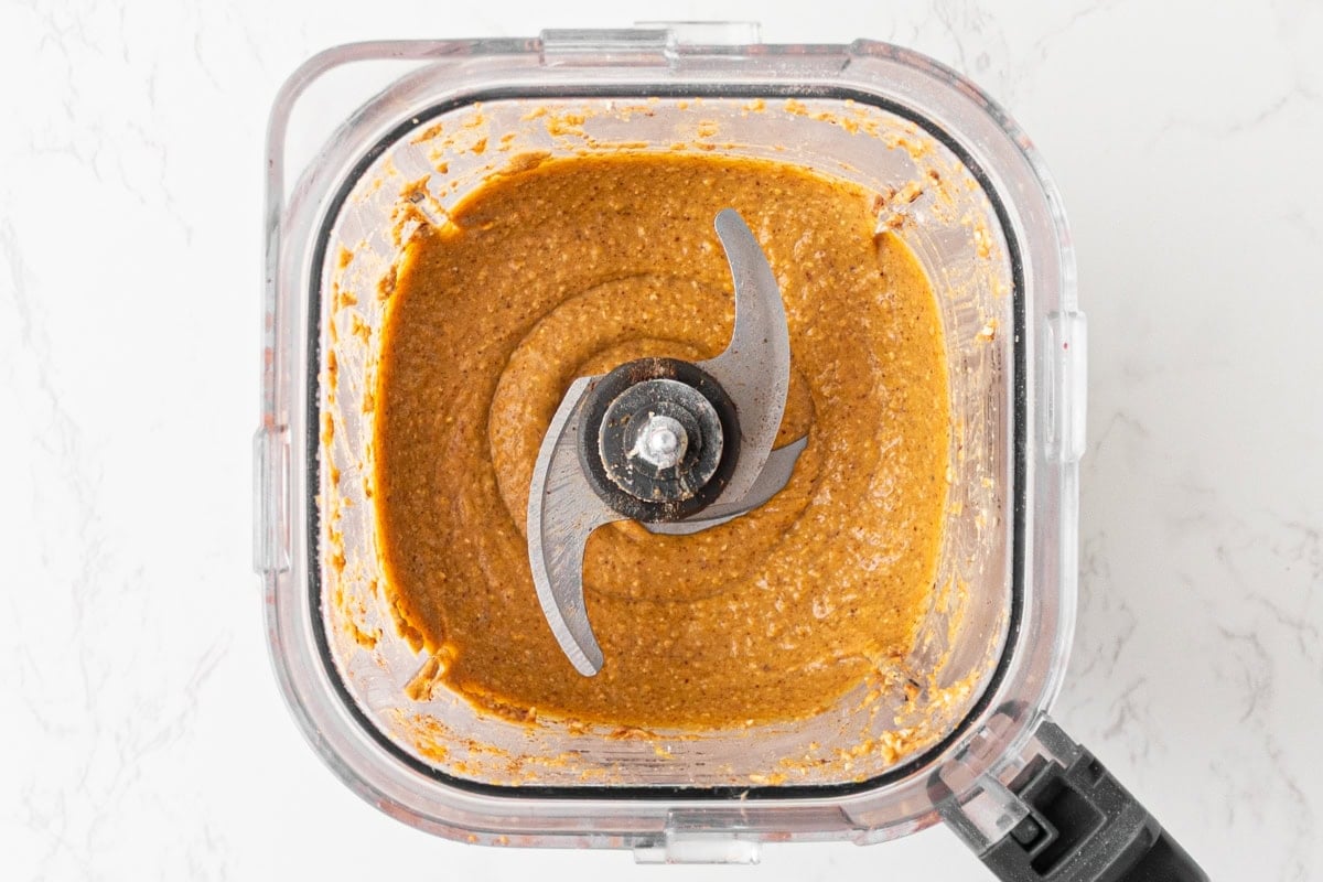Pumpkin, almond butter, eggs, and maple syrup blended into a smooth orange batter base for flourless pumpkin muffins.