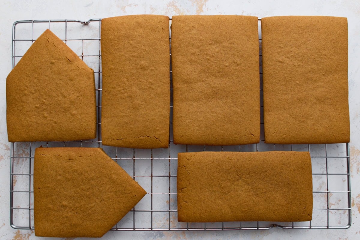 All baked and cooled gingerbread house pieces, including front, back, sides, and roof panels, arranged on a wire cooling rack.