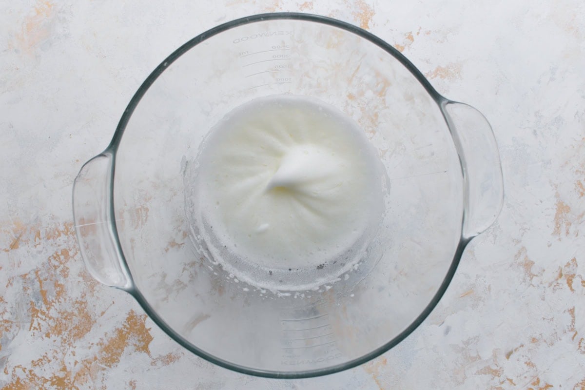A glass bowl with glossy white egg whites beaten until soft peaks form, the start of making royal icing.