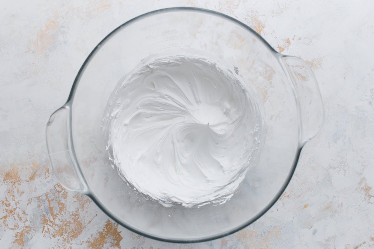 A glass mixing bowl filled with thick, smooth white royal icing whipped to stiff peaks, ready for piping.