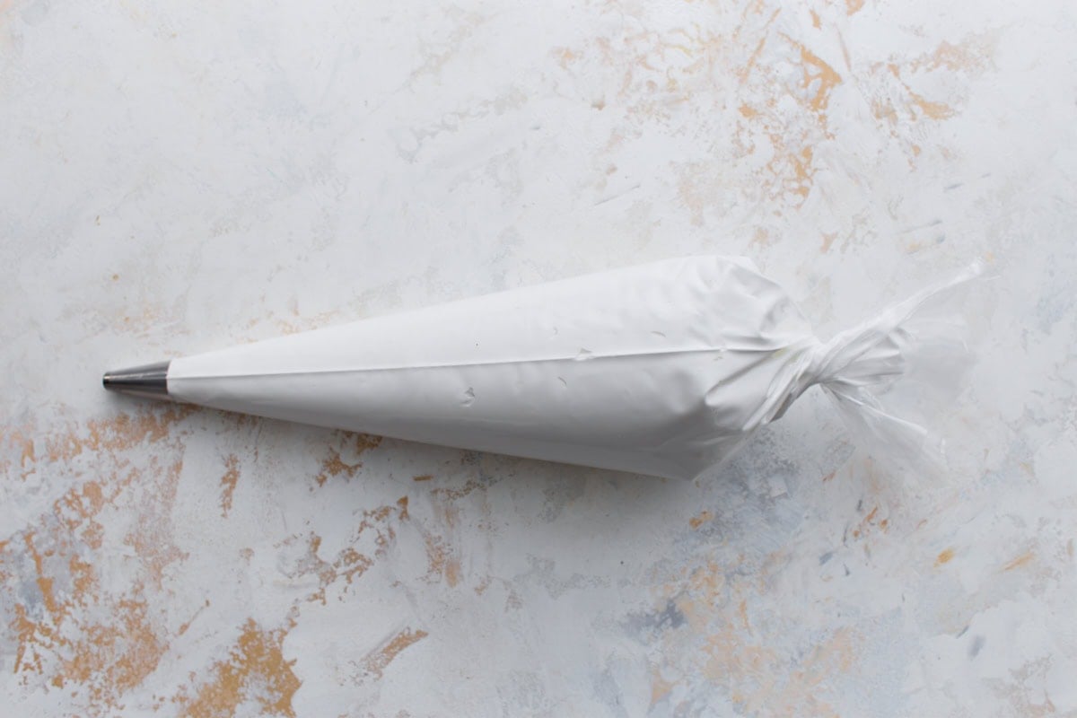 A large piping bag filled with white royal icing and fitted with a metal tip, resting on a light background.