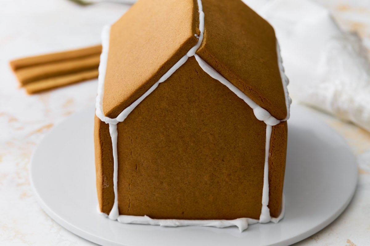 The gingerbread house partially assembled with roof panels attached and seams sealed with white royal icing.