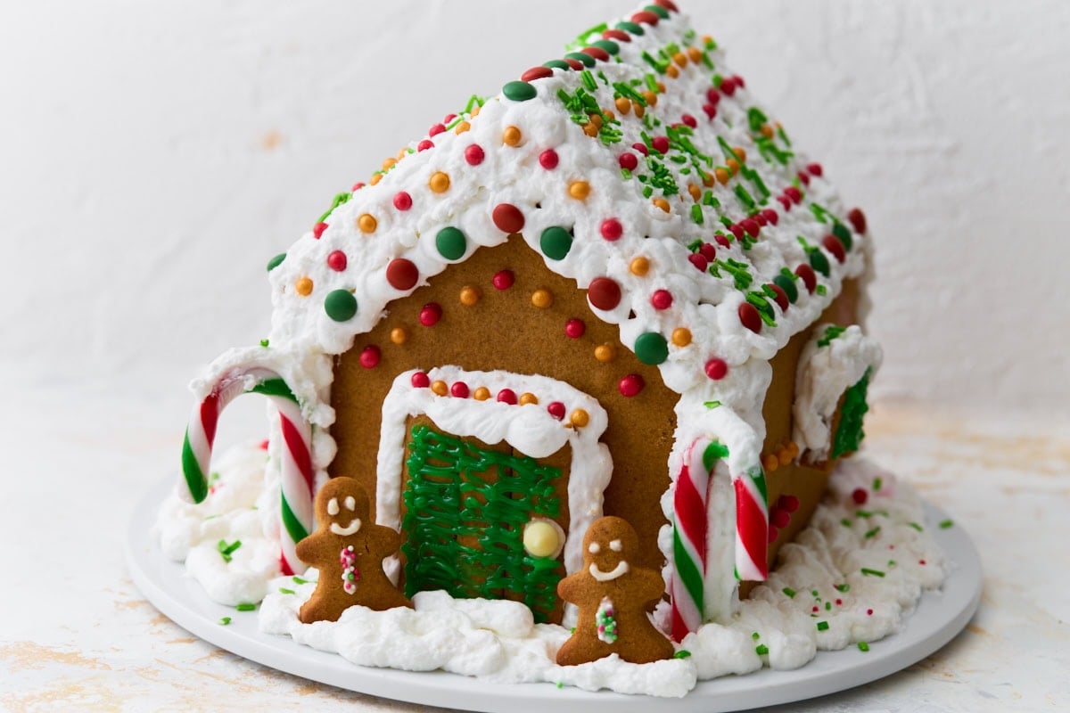 A fully decorated gluten-free gingerbread house with candy canes, colorful candies, and piped white icing viewed from a side angle.