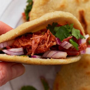 Close-up of a gluten-free gordita filled with shredded chicken, red onions, and fresh cilantro.