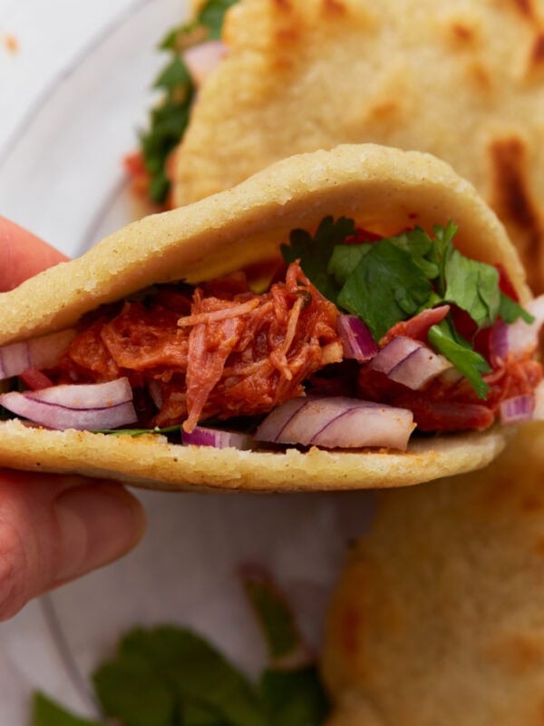 Close-up of a gluten-free gordita filled with shredded chicken, red onions, and fresh cilantro.