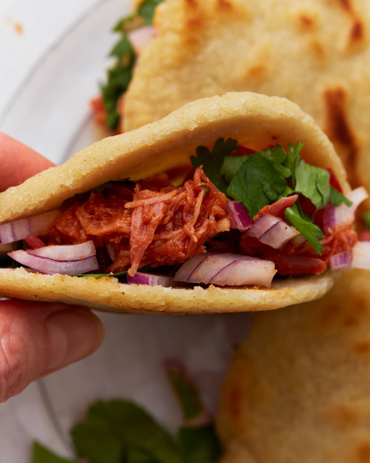 Close-up of a gluten-free gordita filled with shredded chicken, red onions, and fresh cilantro.