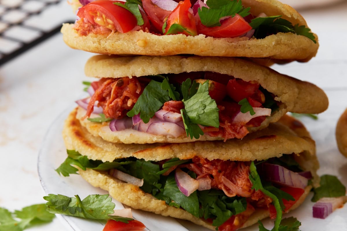 Stack of gluten-free gorditas filled with shredded chicken, tomatoes, red onion, and cilantro.