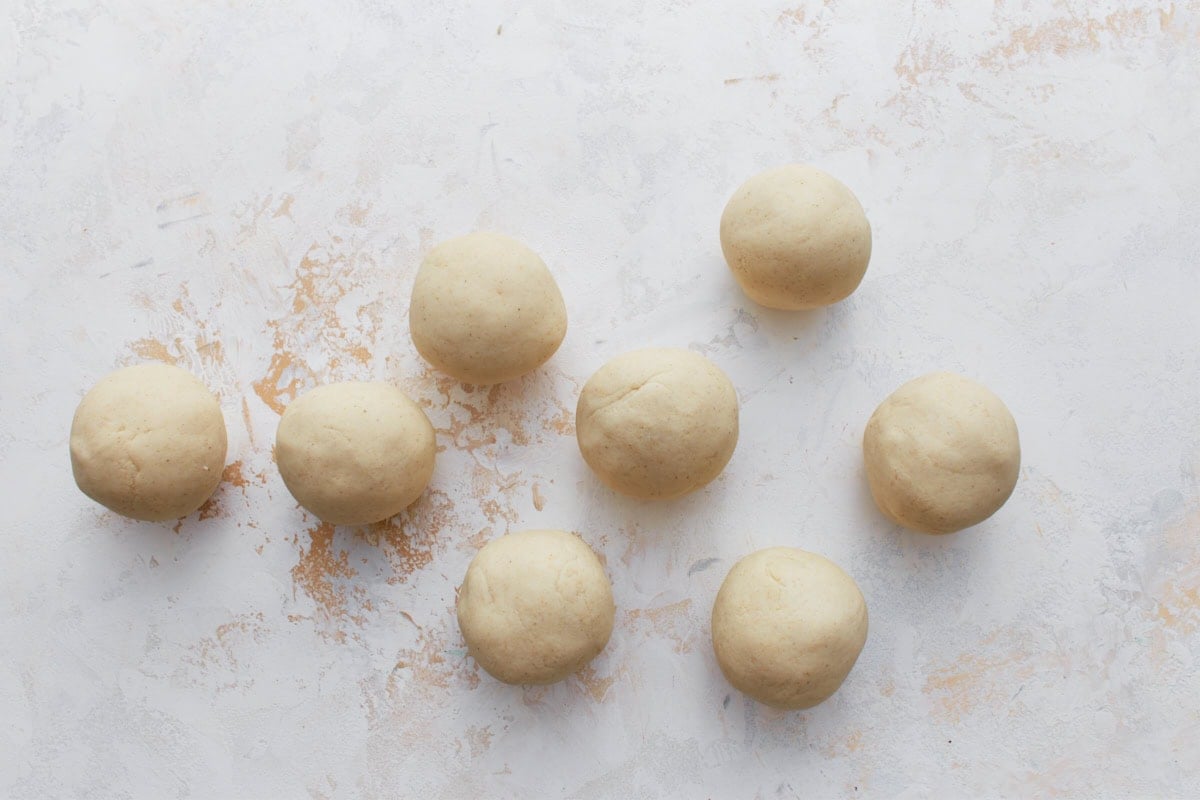 Eight evenly shaped balls of masa dough arranged on a white surface before flattening.