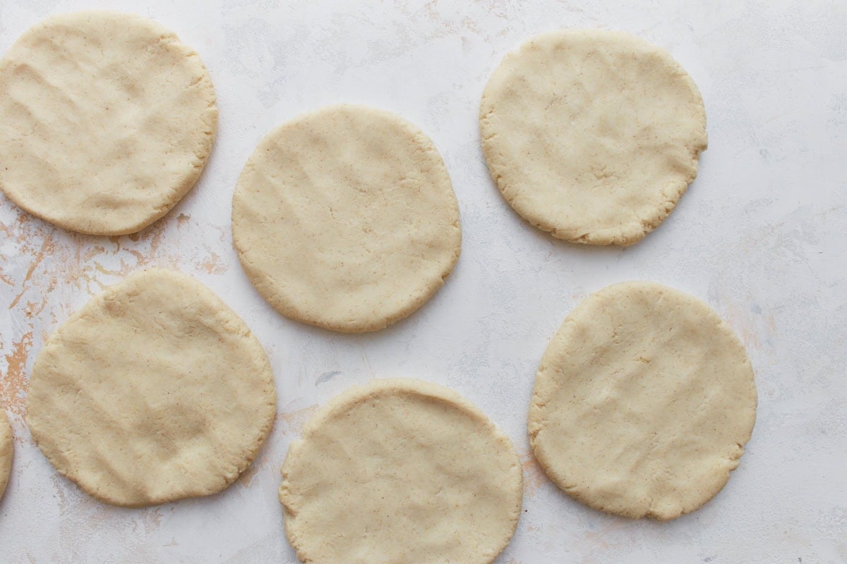 Flattened raw gordita disks of masa dough laid out on a white countertop, ready to cook.