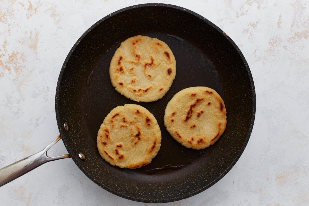 Three gluten-free gorditas cooking in a skillet with golden brown spots forming on top.