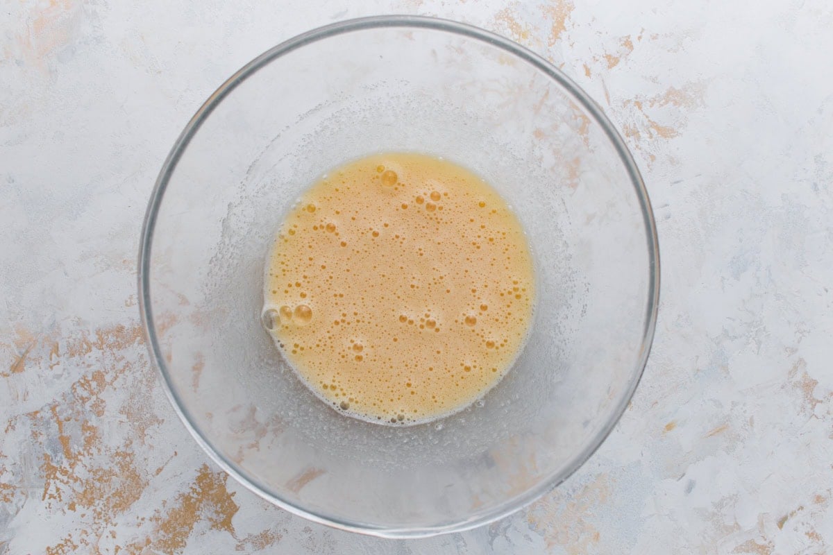 Glass bowl with beaten eggs and sugar mixture, pale yellow and slightly frothy.