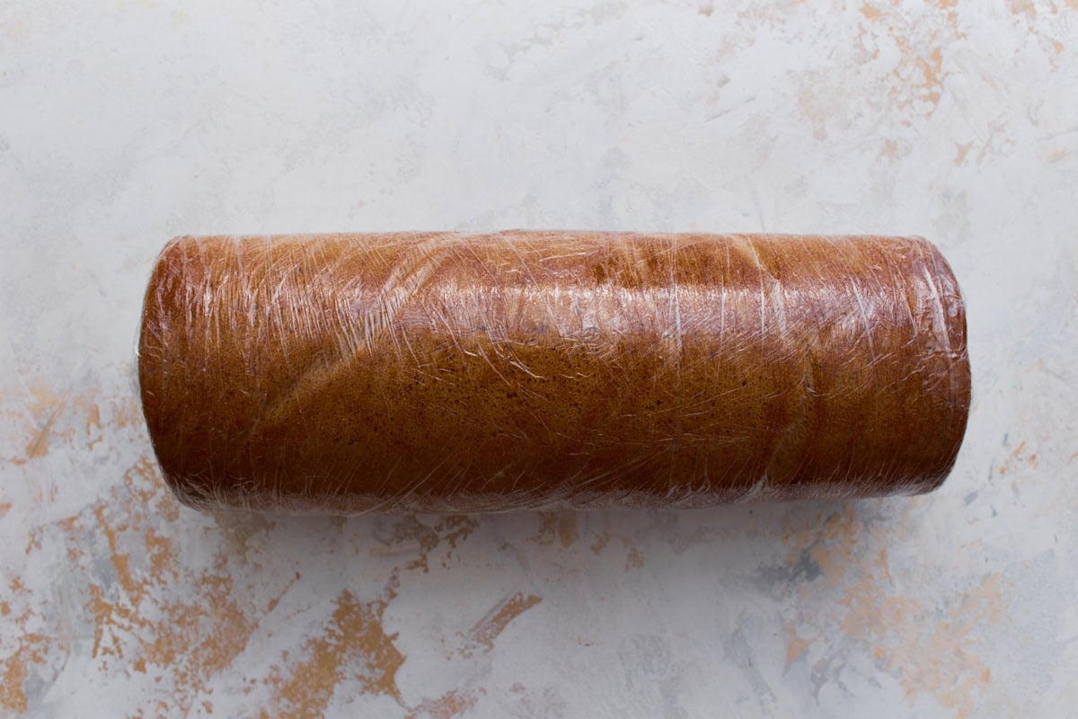 Gluten-free pumpkin roll tightly wrapped in plastic wrap, ready to chill in the refrigerator.