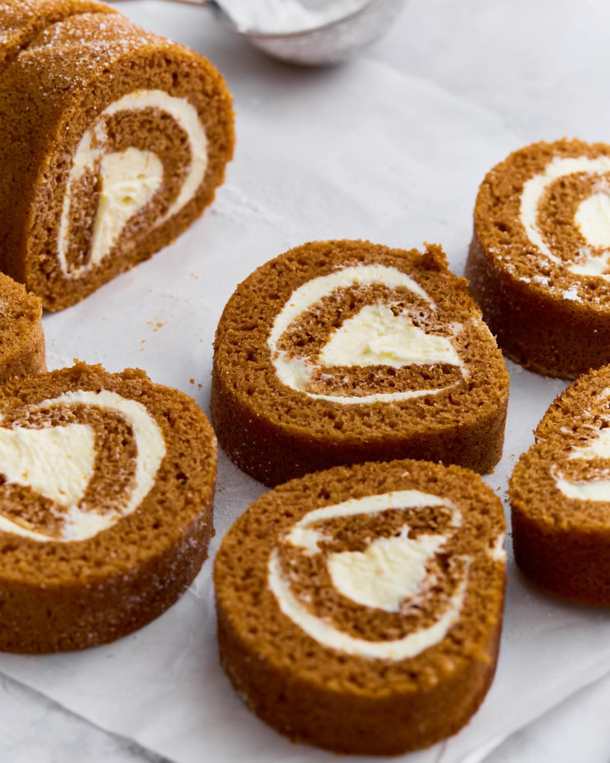 Close-up of gluten-free pumpkin roll sliced into swirls with cream cheese filling, dusted lightly with powdered sugar.