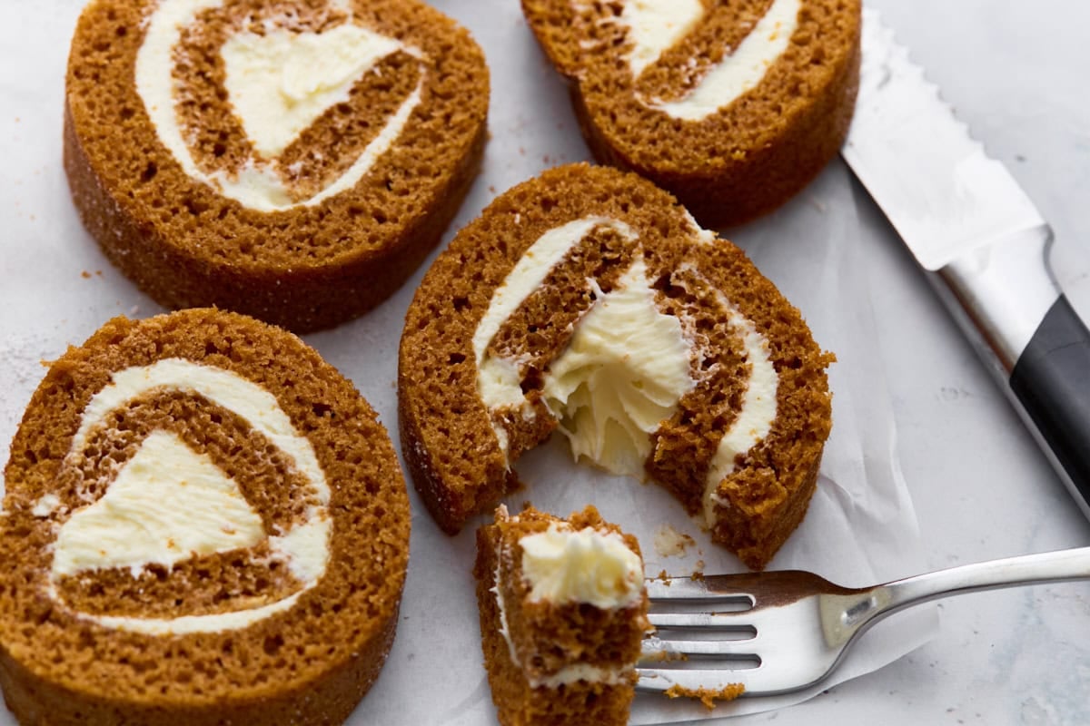 Close-up of pumpkin roll slices on parchment paper with one piece cut into by a fork, highlighting the creamy filling.