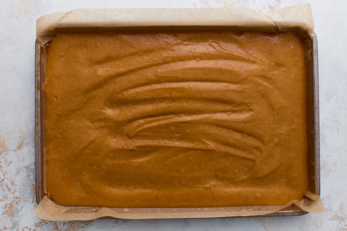 Pumpkin roll batter spread evenly into a parchment-lined jelly roll pan, ready to bake.