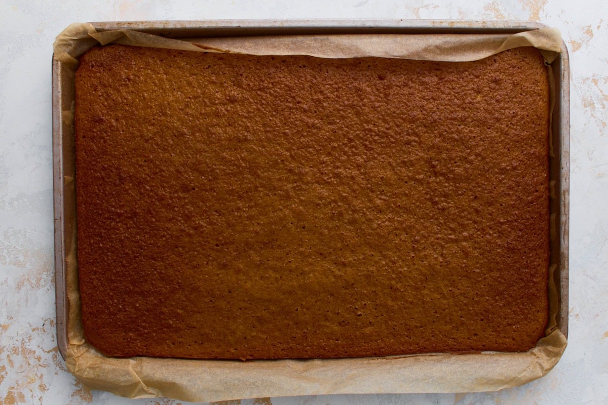 Freshly baked pumpkin roll sponge in the jelly roll pan, golden brown and even in texture.