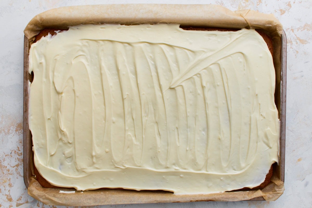 Cooled pumpkin sponge with an even layer of cream cheese frosting spread across the top, ready to roll.