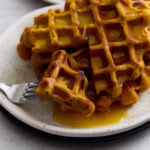 Golden-brown gluten-free pumpkin waffle topped with maple syrup on a white plate with a fork.