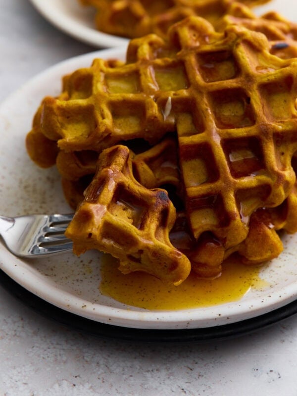 Golden-brown gluten-free pumpkin waffle topped with maple syrup on a white plate with a fork.