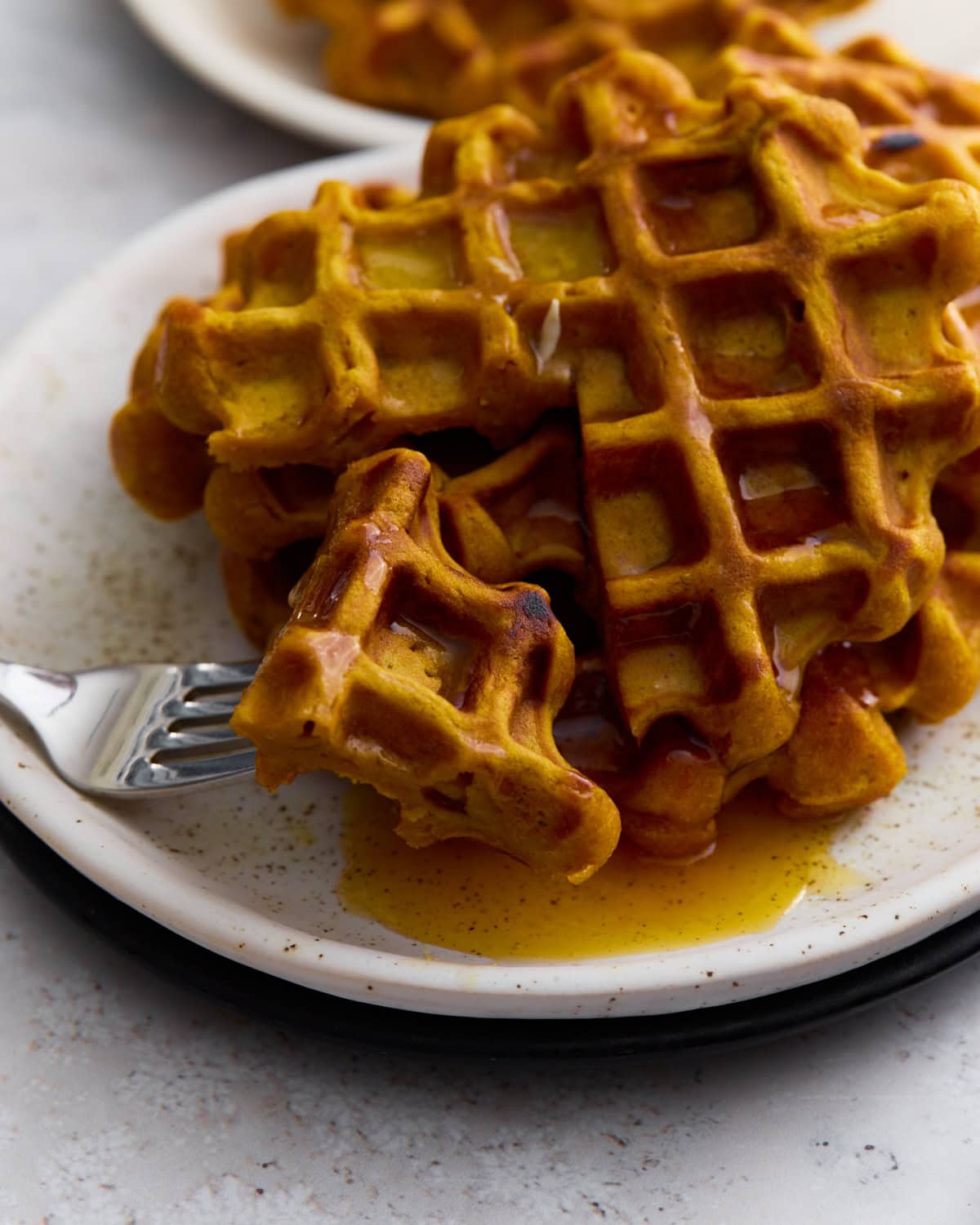 Golden-brown gluten-free pumpkin waffle topped with maple syrup on a white plate with a fork.