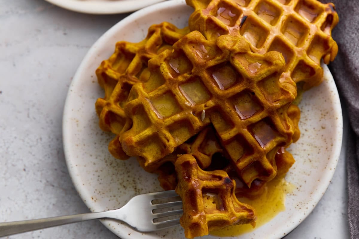 Plate of golden gluten-free pumpkin waffles drizzled with syrup and served with a fork.