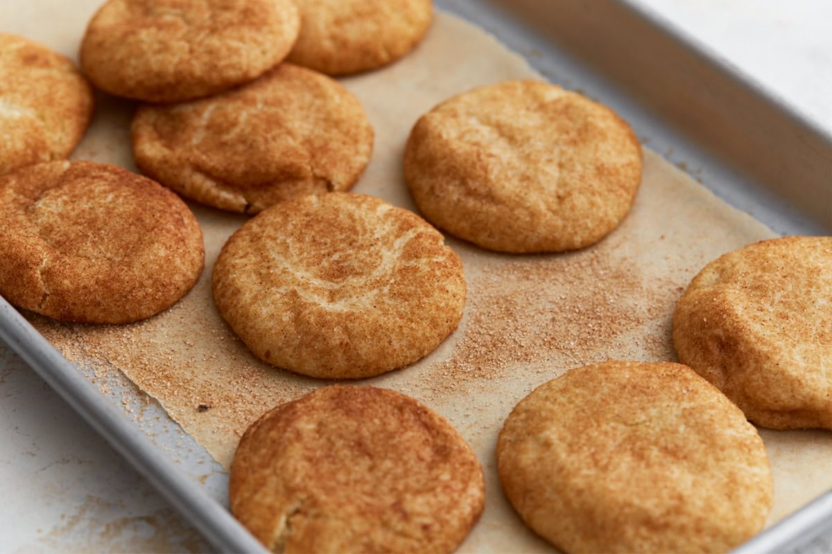 Warm snickerdoodle cookies resting on a parchment-lined pan, highlighting their cinnamon sugar coating and chewy centers.