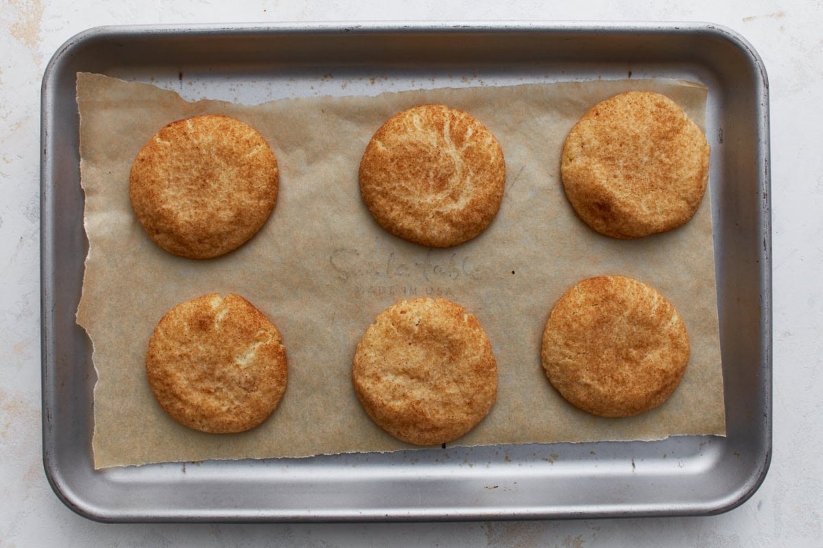 Baked gluten-free snickerdoodle cookies on parchment, evenly golden brown with a soft, crackled top.