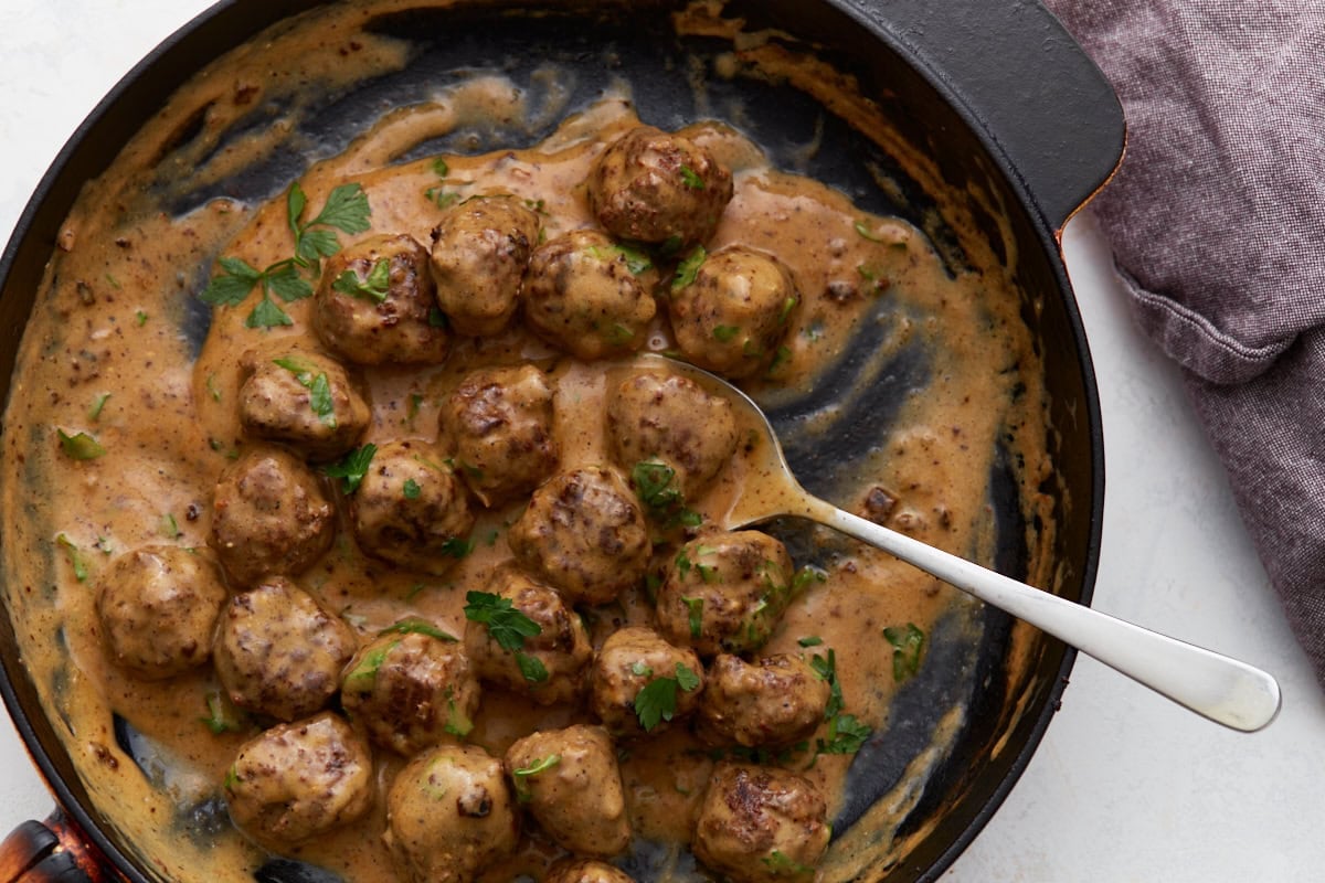 Keto Swedish meatballs coated in creamy sauce with parsley and a serving spoon in the skillet.