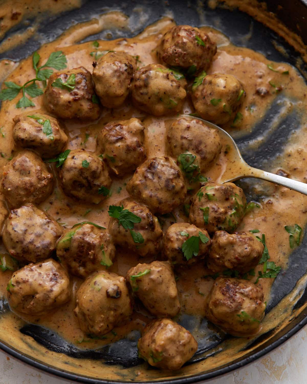 Keto Swedish meatballs in a creamy sauce garnished with fresh parsley in a skillet.