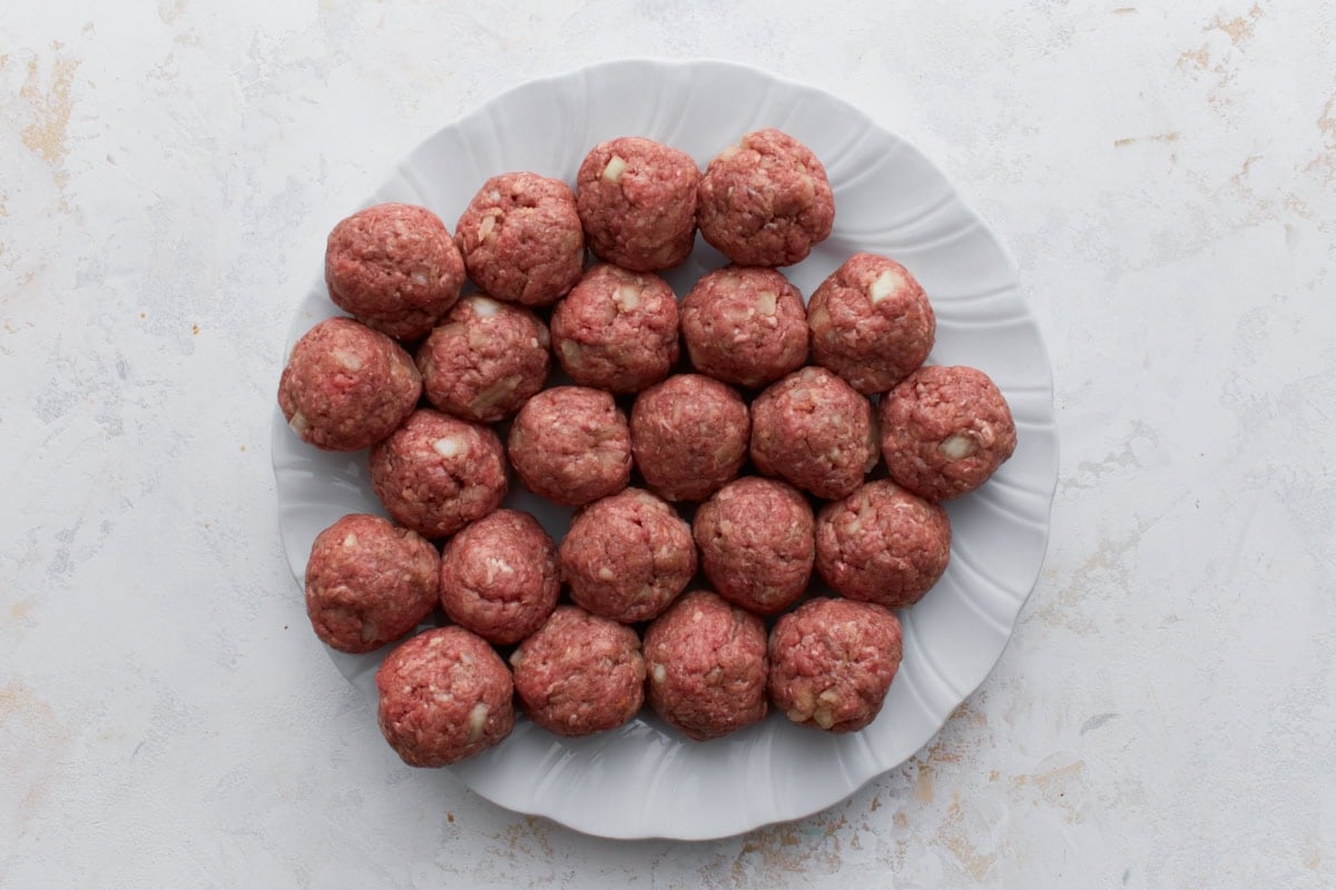Uncooked Swedish meatballs rolled and arranged on a plate before cooking.