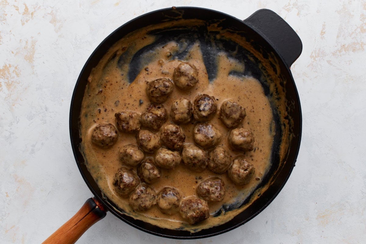 Swedish meatballs simmering in a creamy brown sauce in a black skillet.