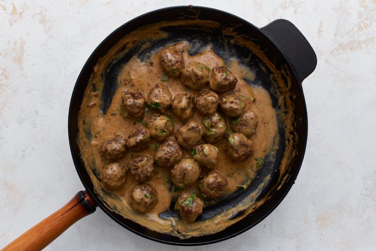 Cooked Swedish meatballs simmering in creamy sauce in a skillet.