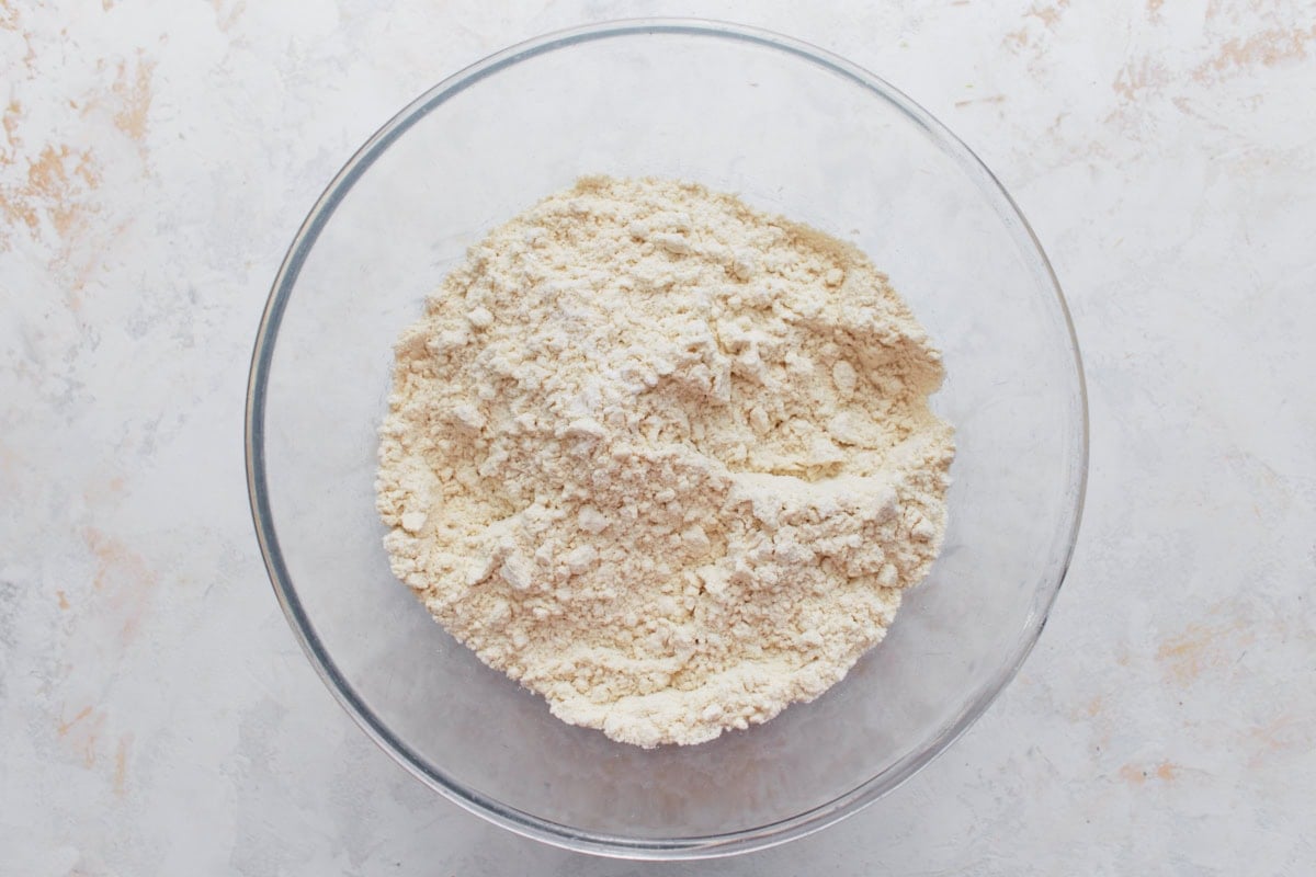 A glass bowl filled with masa harina, baking powder, and salt mixed together for the tamale dough.