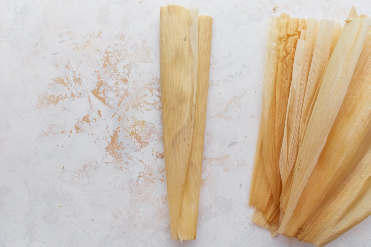 A filled tamale neatly folded and ready for steaming, with extra husks stacked beside it.