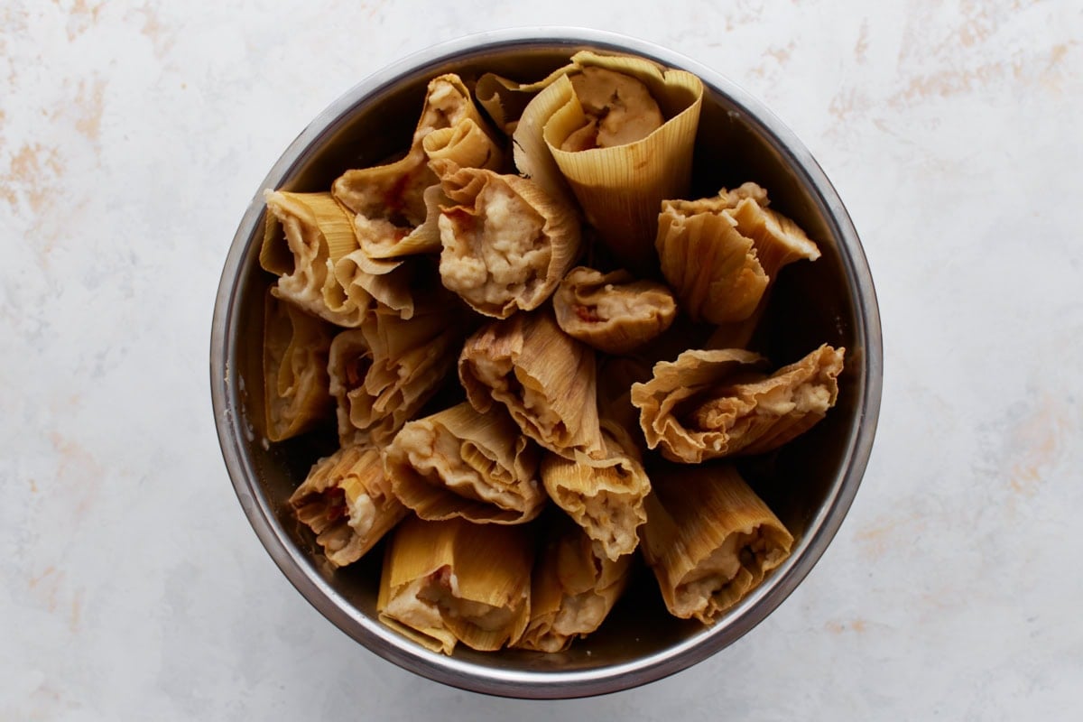 Fully cooked tamales after steaming, with golden husks and firm masa showing at the tops.
