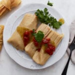 Two gluten-free tamales on a white plate topped with salsa verde and red enchilada sauce, garnished with fresh cilantro.