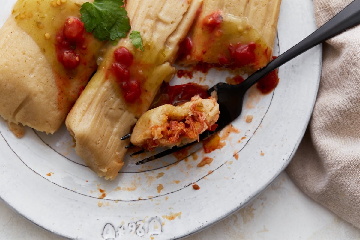 Close-up of a tamale cut open on a fork, showing the red pork filling inside.