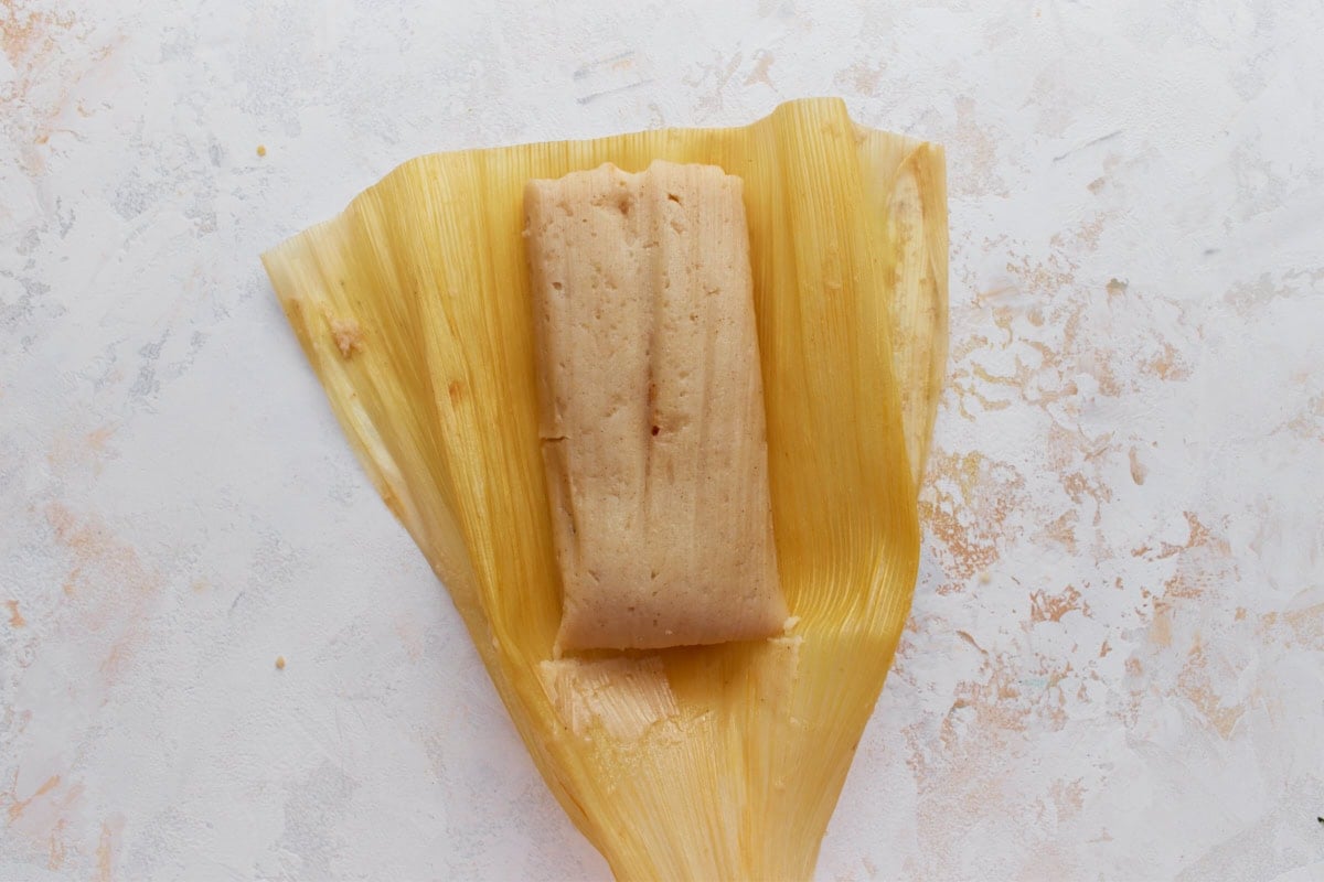 A single cooked tamale unwrapped from the corn husk, showing its soft, smooth masa texture.