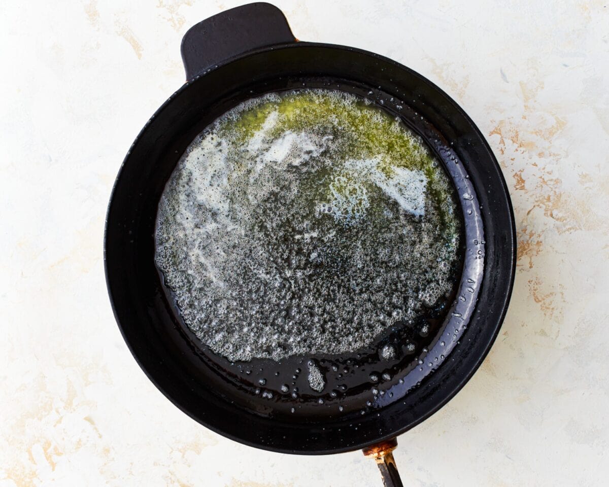 Foamy melted butter coating the bottom of a cast-iron skillet before adding the batter.