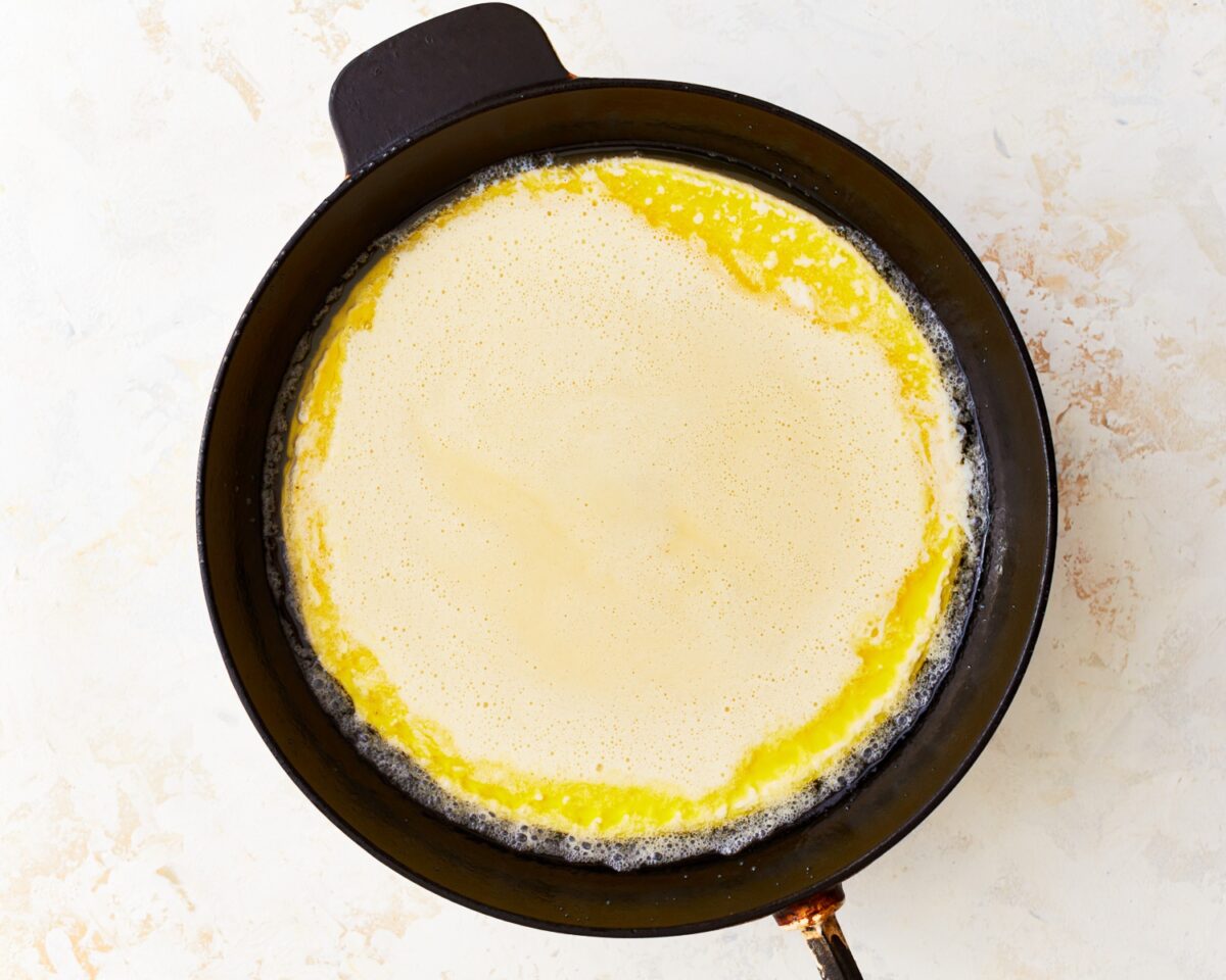 Raw gluten-free Dutch baby batter just poured over melted butter in a hot skillet.