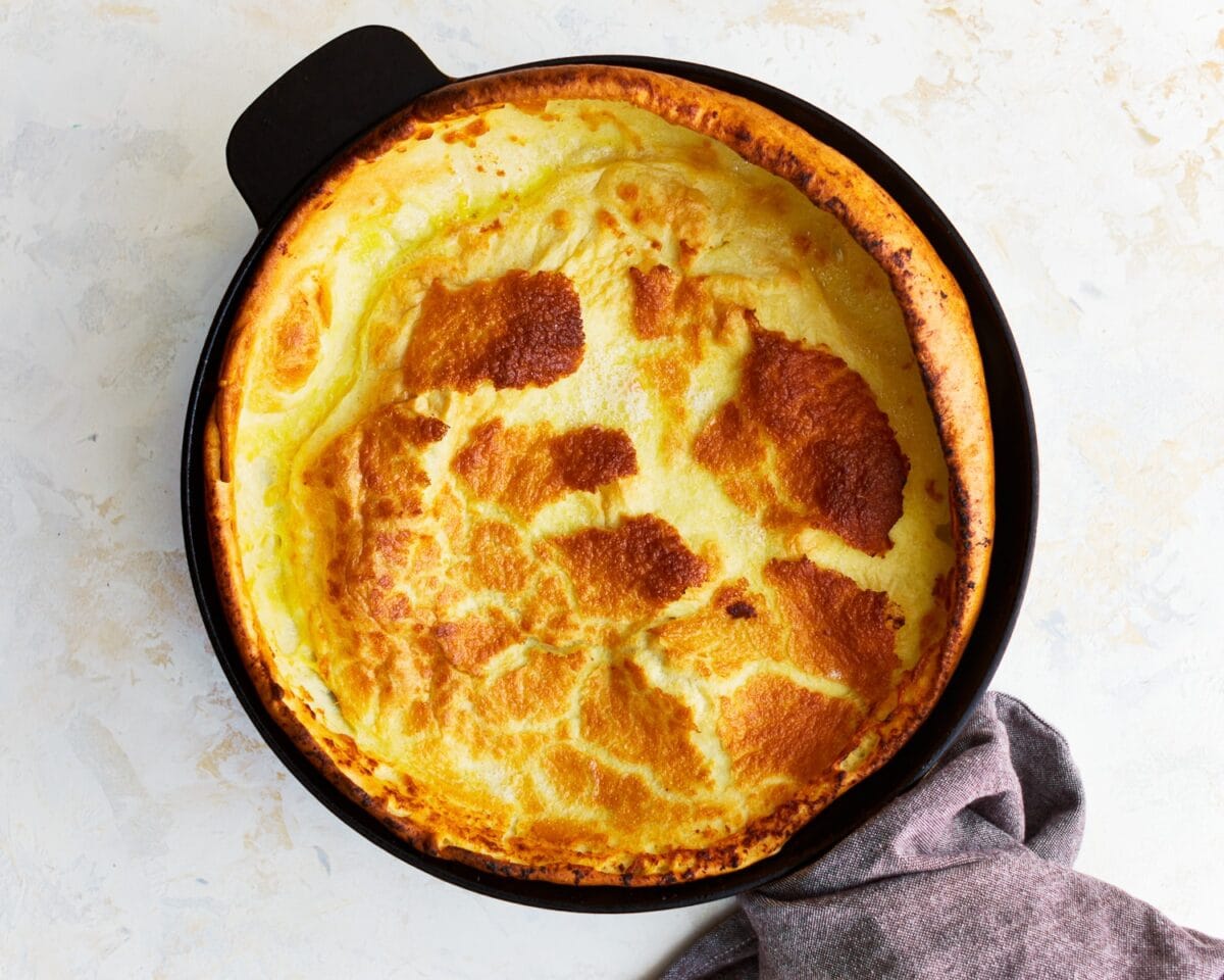 Golden-brown gluten-free Dutch baby pancake puffed up in a cast-iron skillet.