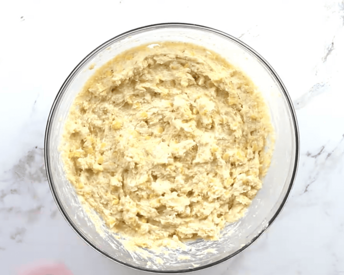 Thick gluten-free corn casserole batter mixed with creamed corn and whole kernel corn in a clear glass bowl.