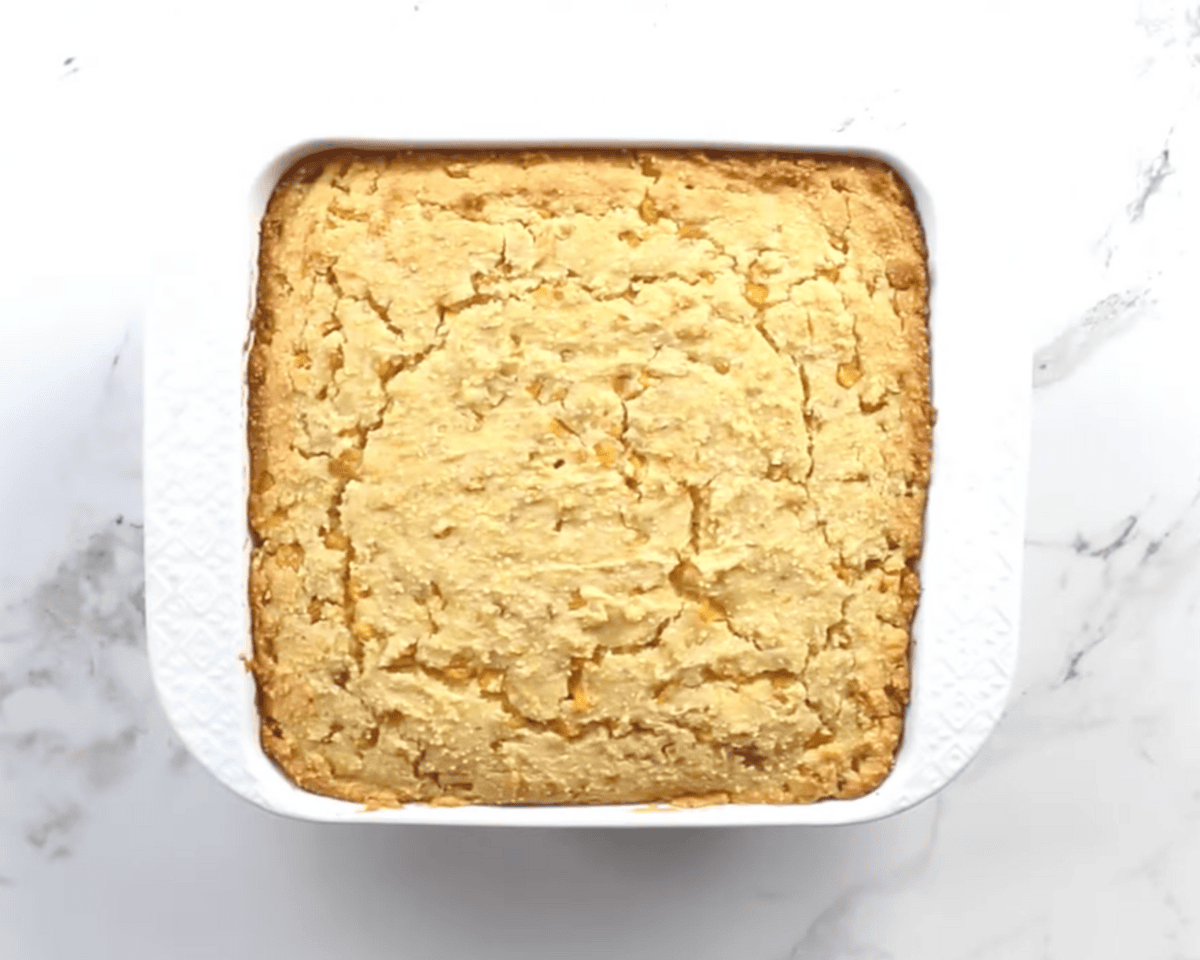 Golden baked gluten-free corn casserole in a square white dish with a lightly cracked, set top.
