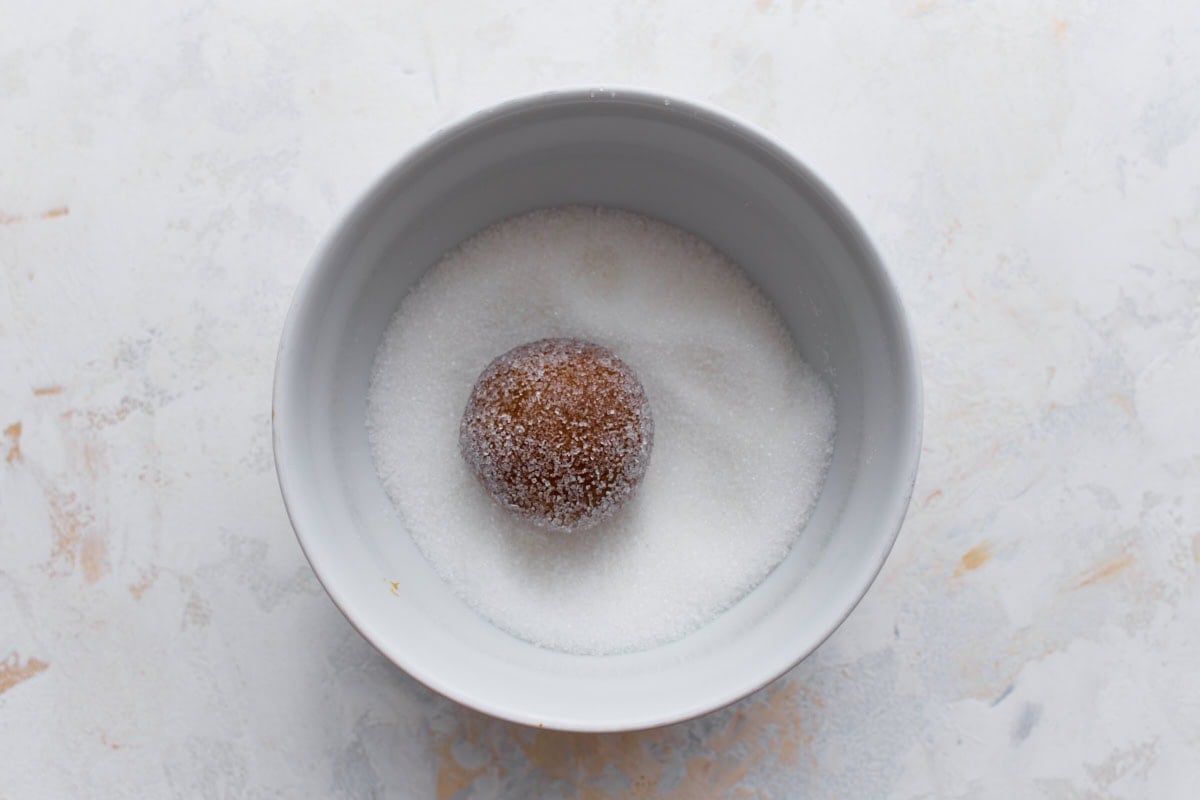 A ball of gingersnap dough being rolled in granulated sugar.