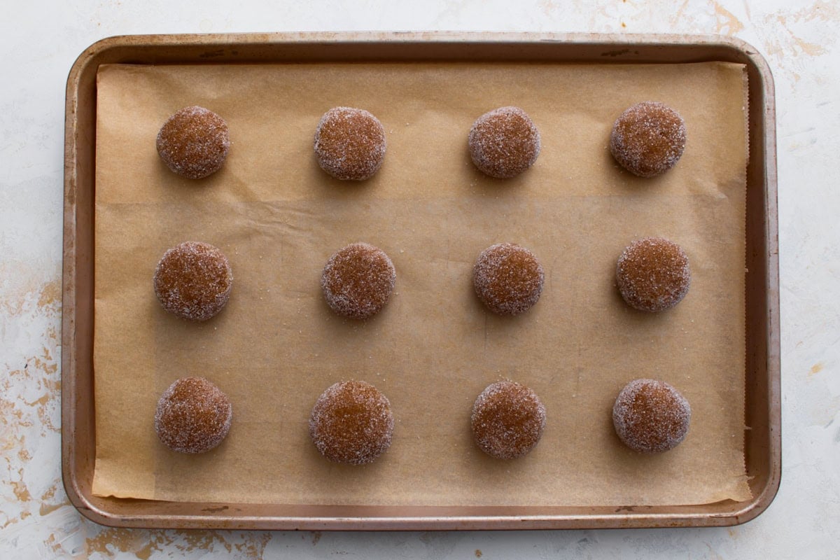 Sugar-coated gingersnap dough balls arranged on a parchment-lined baking sheet.