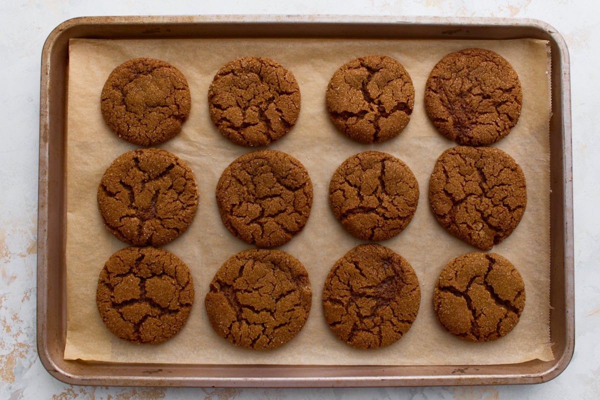 Freshly baked gluten-free gingersnaps cooling on a baking sheet.