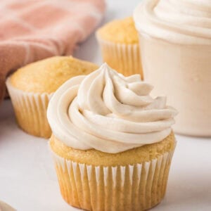 Vanilla cupcake topped with a tall swirl of creamy dairy-free buttercream frosting, with unfrosted cupcakes in the background.