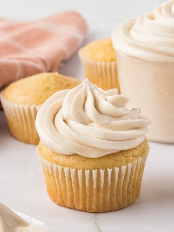 Vanilla cupcake topped with a tall swirl of creamy dairy-free buttercream frosting, with unfrosted cupcakes in the background.