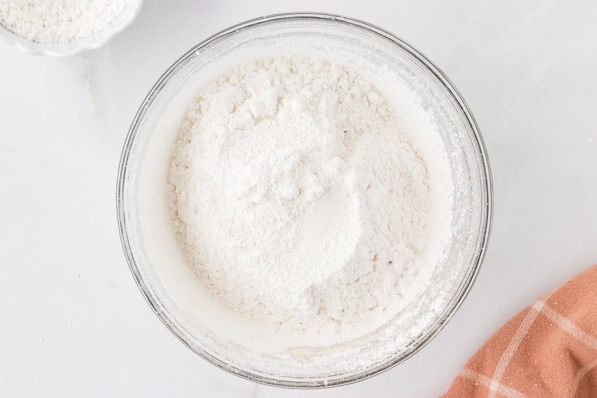 Sifted powdered sugar sitting on top of whipped dairy-free butter in a mixing bowl.