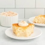 Slice of crustless coconut pie on a white plate topped with whipped cream and toasted coconut.